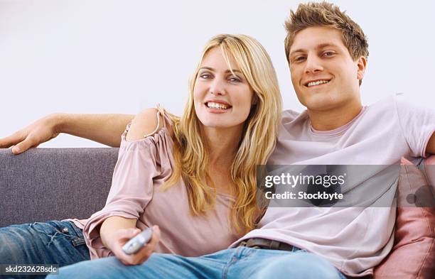 portrait of a young couple sitting on a couch with a remote control - control photos et images de collection