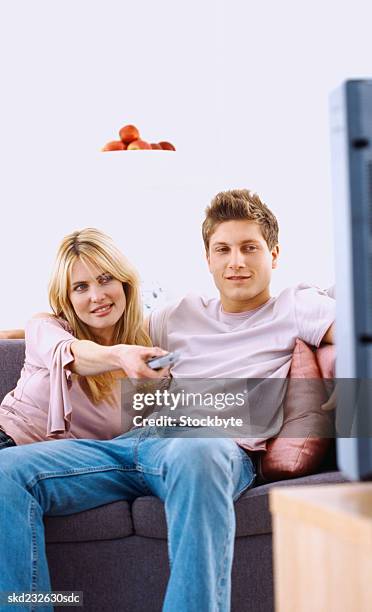 portrait of a young couple sitting on a couch with a remote control - control photos et images de collection