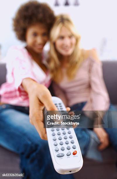 close-up of two young women sitting on a couch with a remote control (blurred) - control photos et images de collection