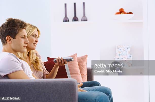 side profile of a young couple sitting on a couch with a remote control - control photos et images de collection