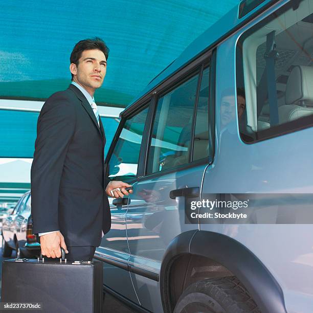 close-up of businessman holding briefcase and opening door of jeep - door stockfoto's en -beelden