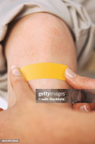 close-up of a woman's hand applying a bandage to a boy's arm - applying bandaid stock pictures, royalty-free photos & images