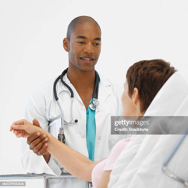 young doctor taking mature patient's pulse - bedside-manner stock pictures, royalty-free photos & images