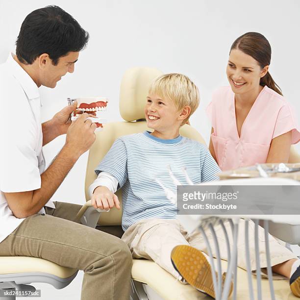 close-up of dentist and dental nurse showing boy how to wash his teeth using model teeth (10-11) - how fotografías e imágenes de stock
