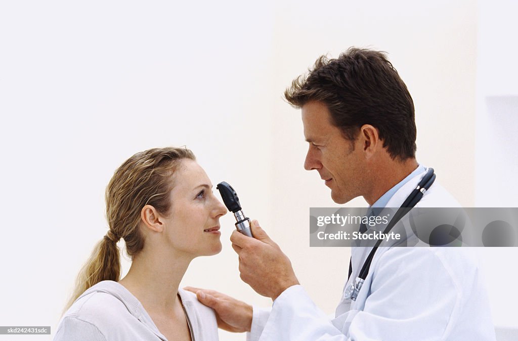 Side profile of a male doctor checking a woman's eye with an ophthalmoscope