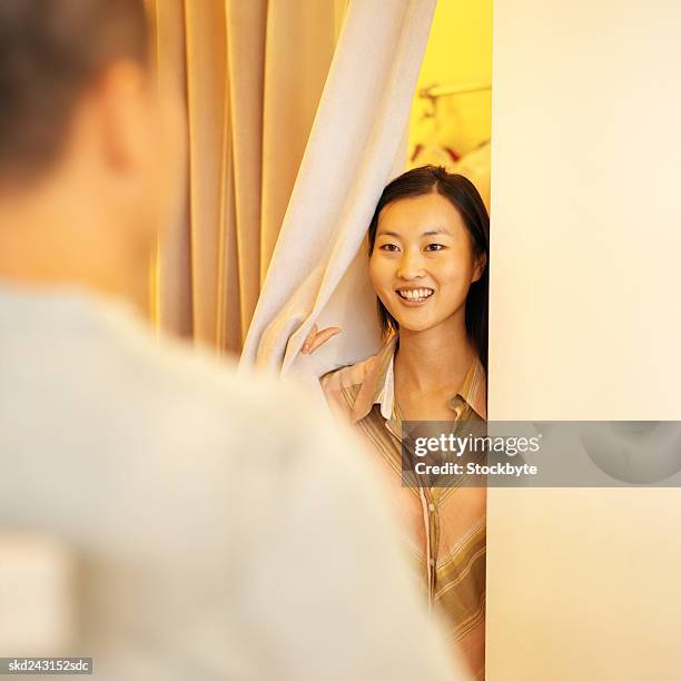 young woman peeping out through dressing room talking to young man - dressing up ストックフォトと画像