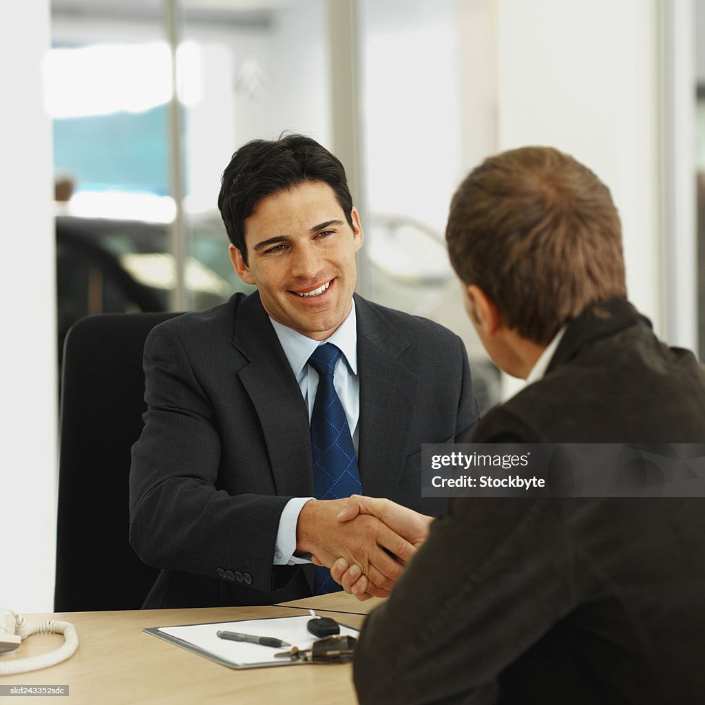 Close-up of salesman and customer shaking hands in office