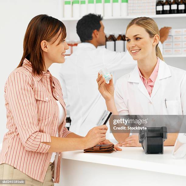 close-up of female pharmacist showing container of tablets to patient with male pharmacist in background - close up counter ストックフォトと画像