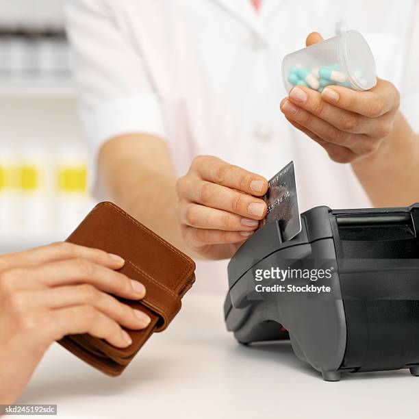 close-up mid section of pharmacist processing credit card into credit card reader with patient beside her - e reader - fotografias e filmes do acervo