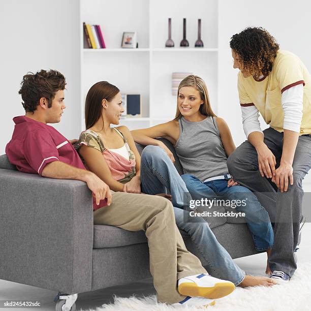 four young people sitting in living room relaxing - living stock-fotos und bilder