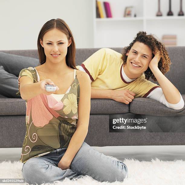 front view of young man lying on sofa with young woman holding remote control - control photos et images de collection