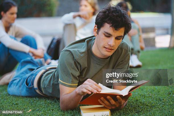 close-up of a young man lying on a lawn and reading - hinge joint stock pictures, royalty-free photos & images