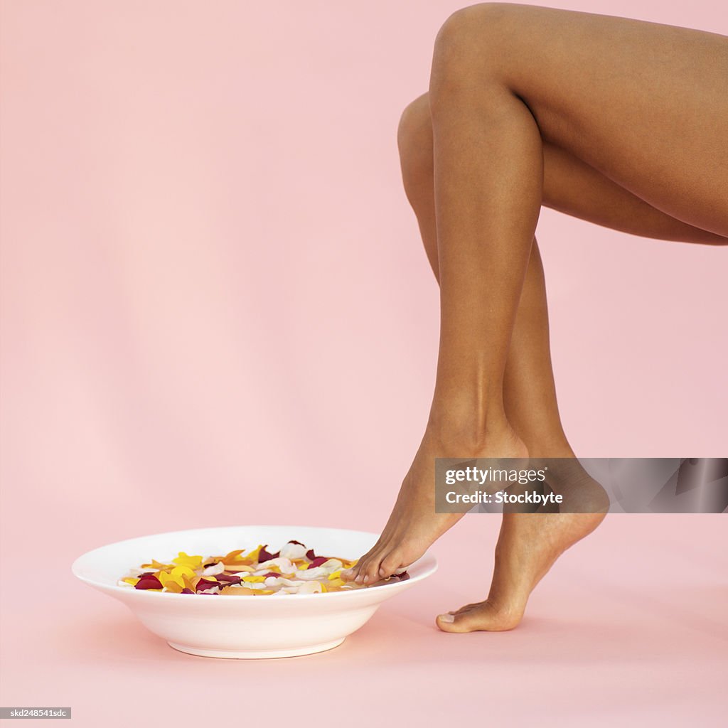 A woman's feet in a bowl of water filled with flower petals