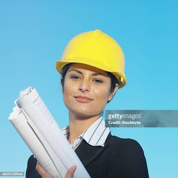 front view portrait of businesswoman wearing hard hat and holding blueprint - hat stock-fotos und bilder