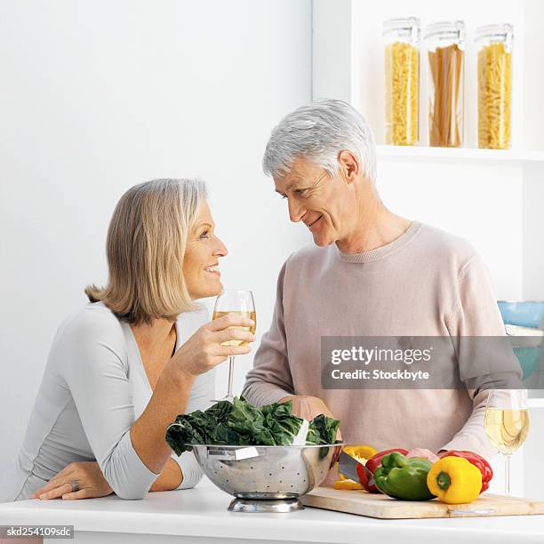 close-up side view of mature man cutting bell peppers with mature woman holding glass of wine - bell stock-fotos und bilder