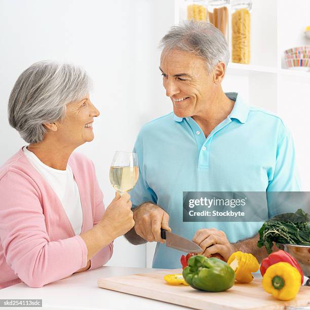 close-up side view of mature man cutting bell peppers with mature woman holding glass of wine - bell foto e immagini stock