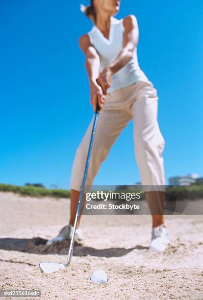 low angle view of a young woman putting from a sand bunker on a golf course - golf bunker low angle stock pictures, royalty-free photos & images