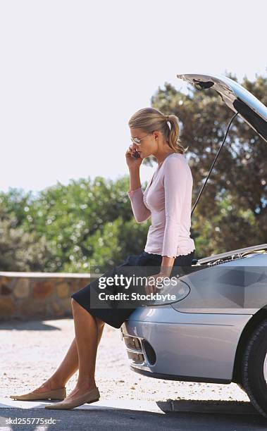 woman standing leaning against a car talking on a mobile phone - vehicle breakdown ストックフォトと画像