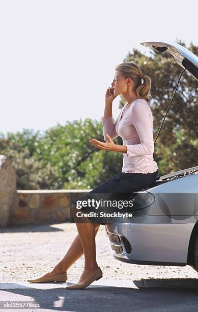 woman standing leaning against a car talking on a mobile phone - vehicle breakdown imagens e fotografias de stock