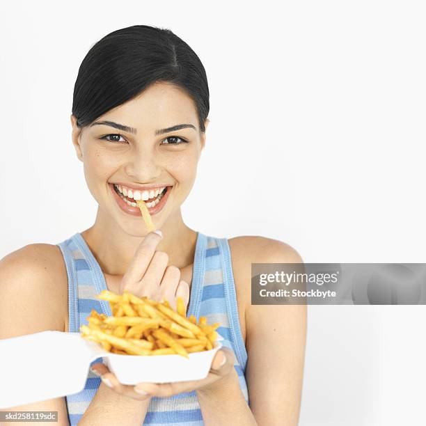 front view of young woman eating carton of french fries - frites stock pictures, royalty-free photos & images