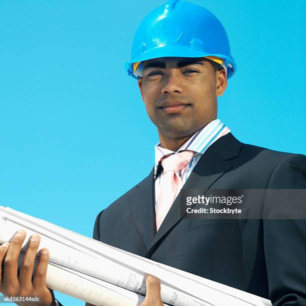 front view portrait of businessman wearing hard hat and holding blueprint - hat stock-fotos und bilder