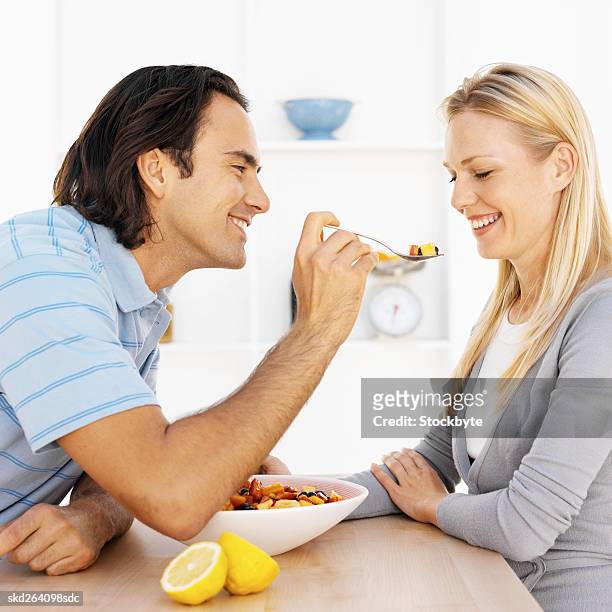 close-up side view of young man feeding young woman spoon of fruit salad - side salad stock pictures, royalty-free photos & images
