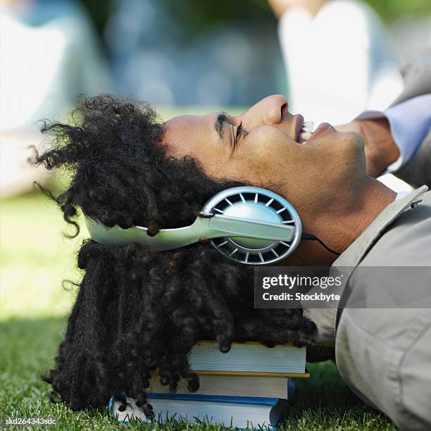 close-up side view of young man lying on grass wearing headphones with head resting on stack of books - african american culture stock pictures, royalty-free photos & images