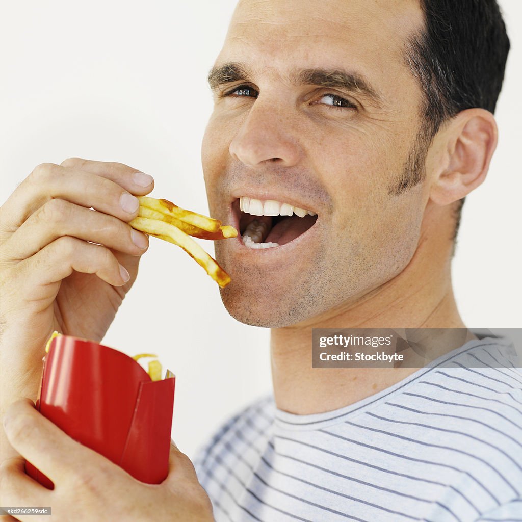 Front view of mid adult man eating French fries