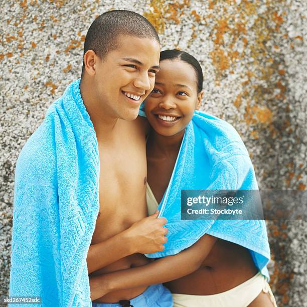 close-up of young couple with arms around each other and holding towel between them - between stock-fotos und bilder