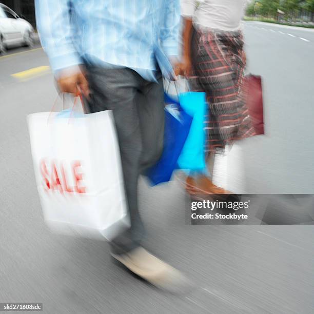 close-up low section of couple walking across the street carrying shopping bags - across stock pictures, royalty-free photos & images