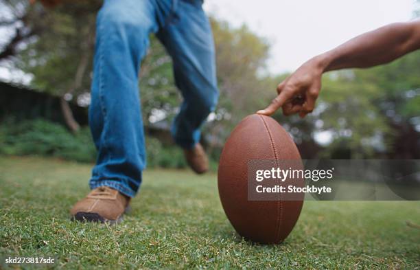 man holding an american football in place for another man to kick - aother stock pictures, royalty-free photos & images