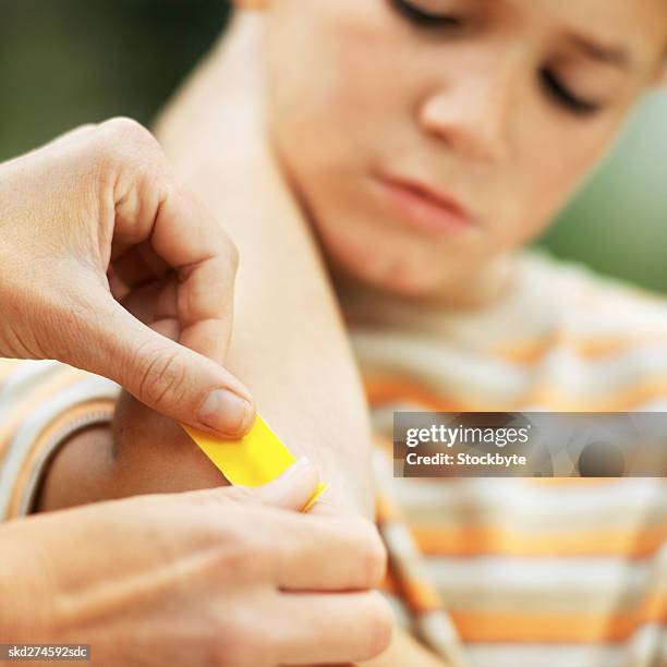 close-up of mother putting plaster on son's elbow (10-11) - hinge joint stock pictures, royalty-free photos & images
