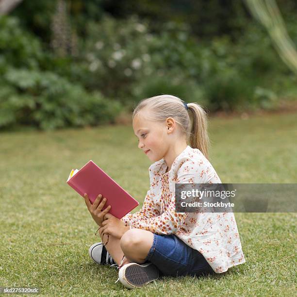 side view of girl reading book in garden (8-9) - fille lire gazon photos et images de collection