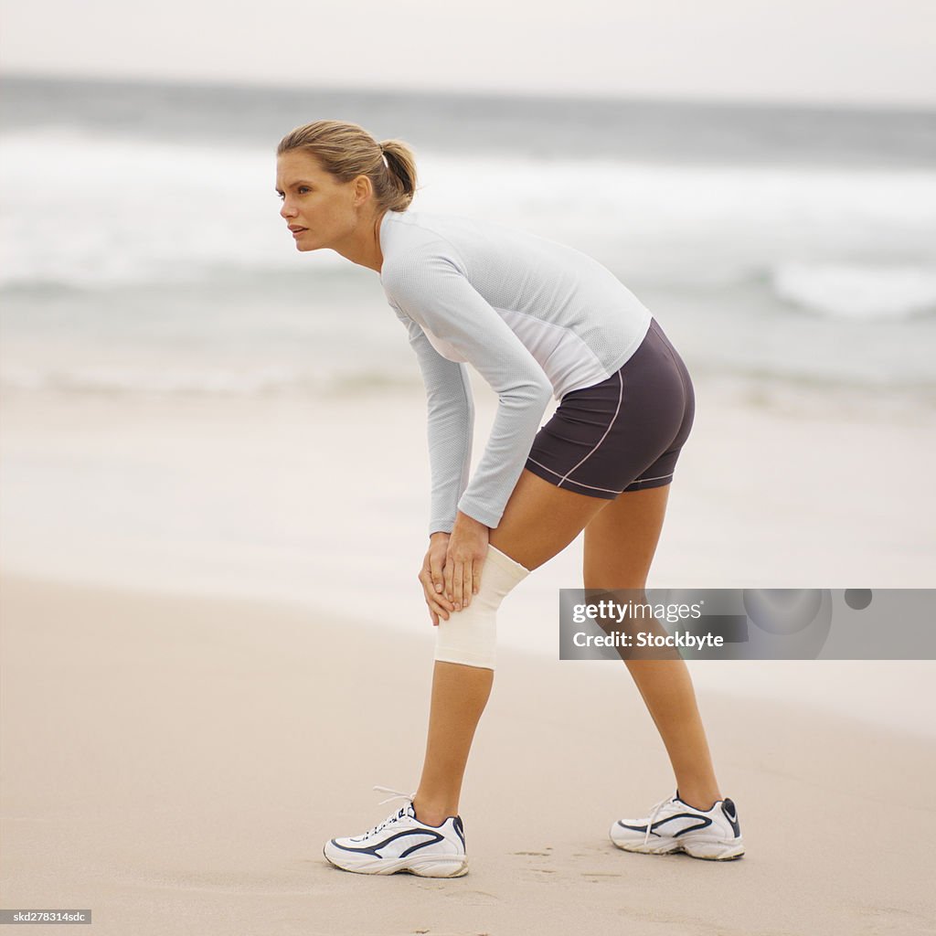 Side view of a concerned woman wearing a knee support holding her knee