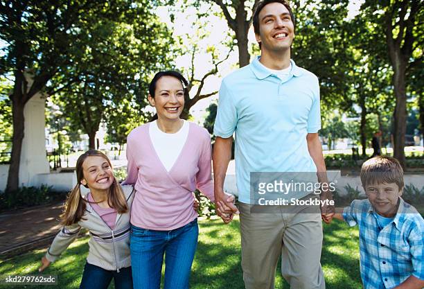 portrait of a couple walking with their children (6-8) across a lawn - across stock pictures, royalty-free photos & images