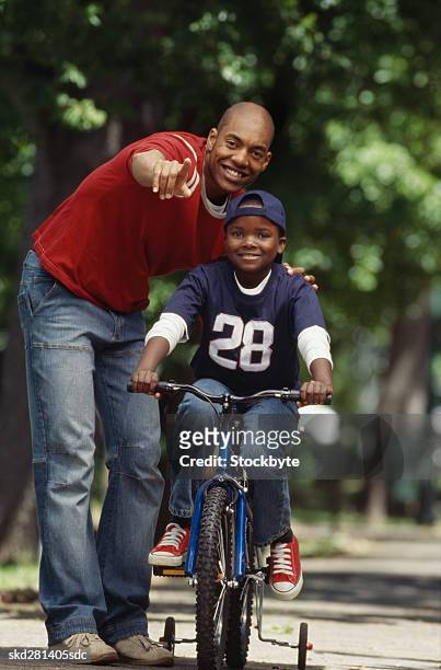 front view portrait of father teaching son how to cycle bicycle (10-11) - how fotografías e imágenes de stock