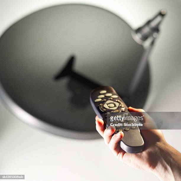 close-up of man's hand holding remote control with satellite dish in background - control photos et images de collection