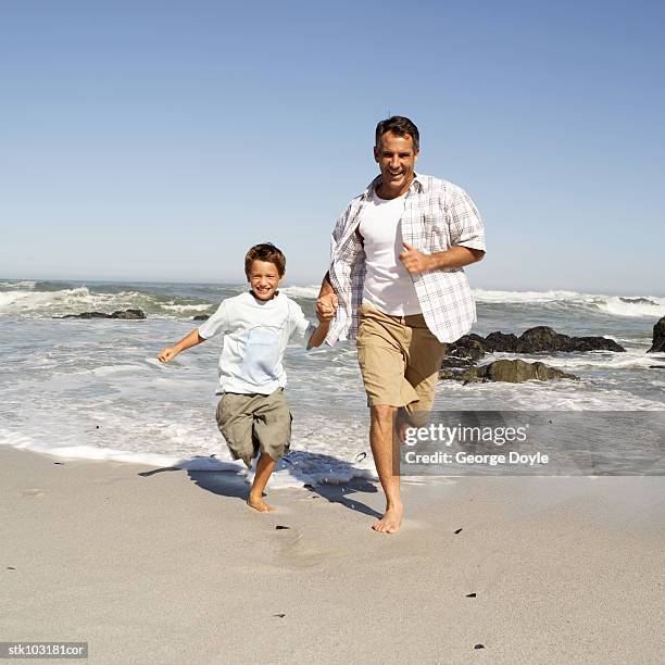 portrait of a father and son running at the beach - intergénero fotografías e imágenes de stock