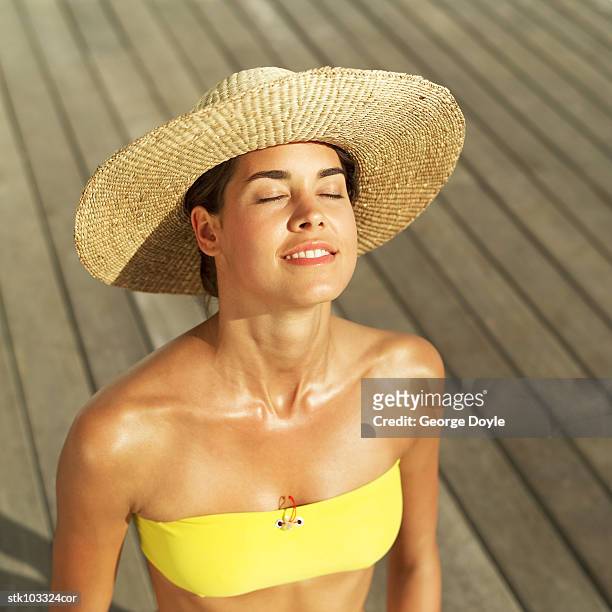 woman sitting with eyes closed wearing a straw hat - hat stock-fotos und bilder