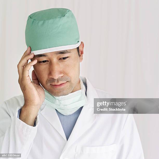 male surgeon wearing scrubs standing with his hand on his head - hand on head ストックフォトと画像