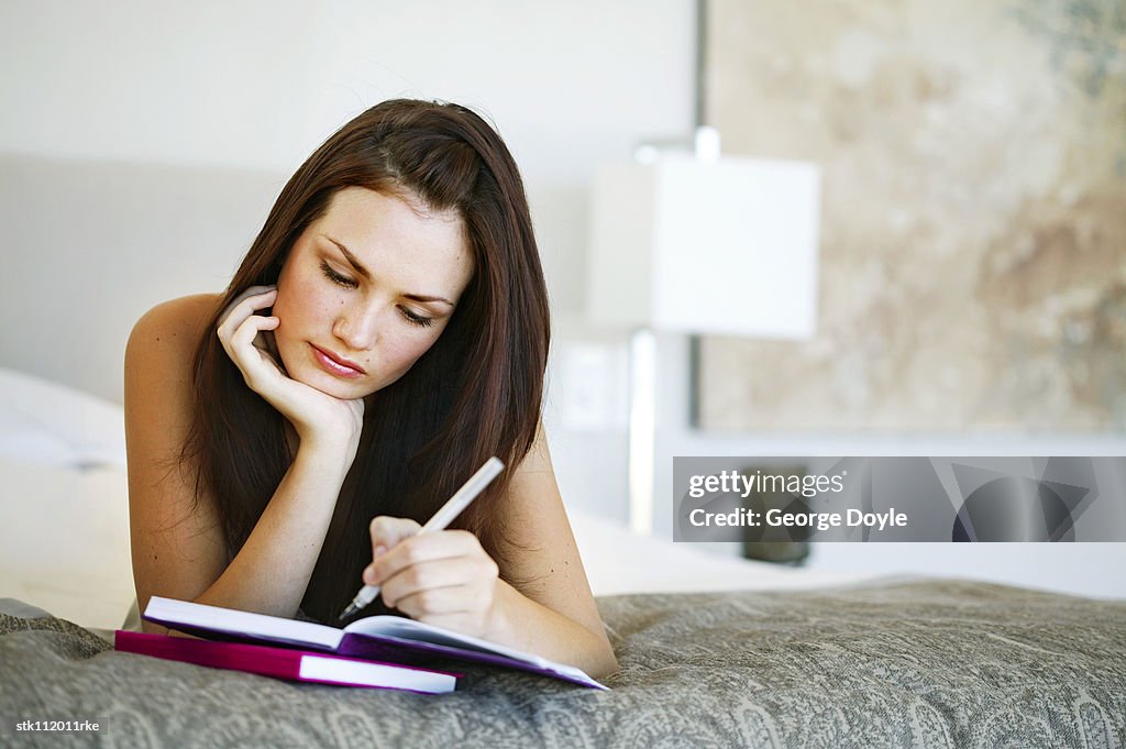 Young woman lying on a bed writing in a notebook