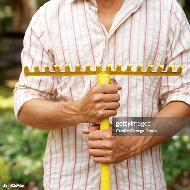 portrait of a person standing grasping a rake in his hands - rake stock-fotos und bilder