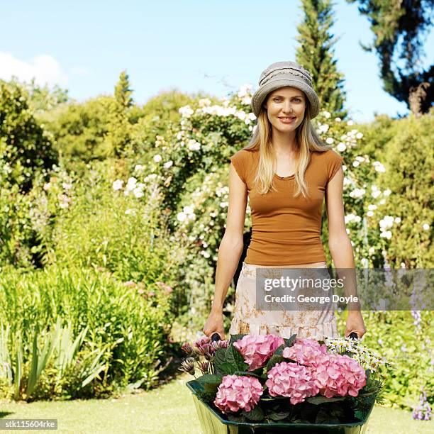 portrait of a young girl pushing a wheelbarrow with potted plants - temperate flower imagens e fotografias de stock