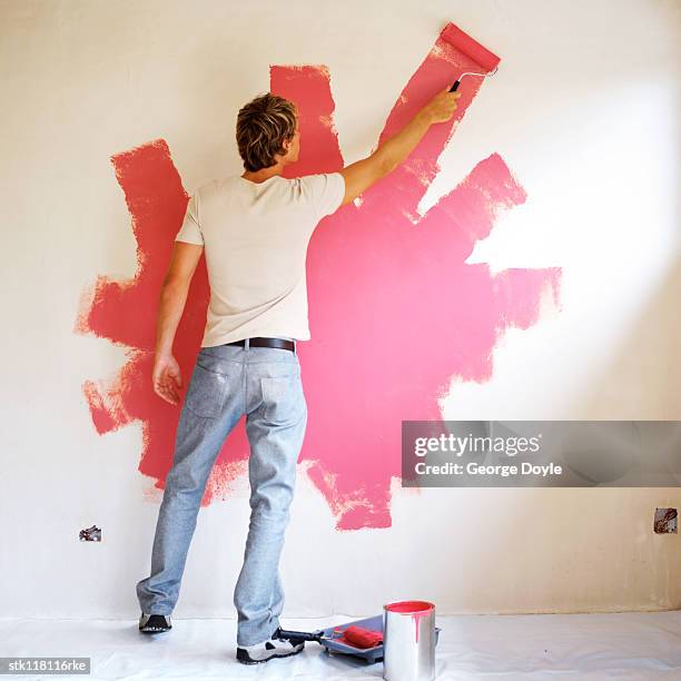 young man painting a wall with a paint roller - roller fotografías e imágenes de stock