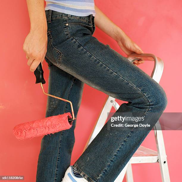 side profile of a young woman standing on a ladder with a paint roller brush - roller fotografías e imágenes de stock