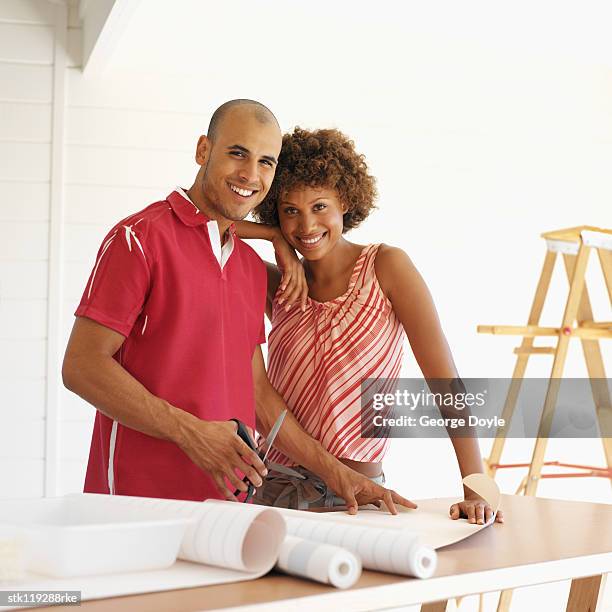 portrait of a young couple cutting wallpaper together - hinge joint stock pictures, royalty-free photos & images