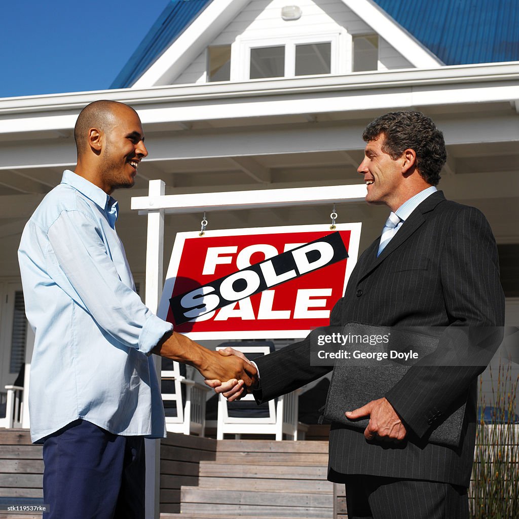 Side profile of a male real estate agent shaking hands with a young man