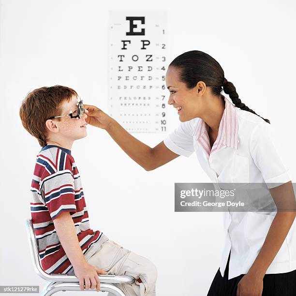 side profile of a female optometrist examining a boy's (8-10) eyes - phoroptor stock pictures, royalty-free photos & images