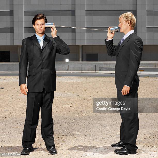 two young businessmen talking listening with tin cans and string - string - fotografias e filmes do acervo