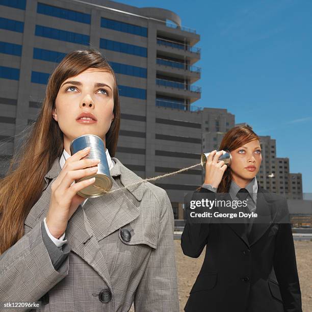 two young businesswomen talking listening with tin cans and string - string - fotografias e filmes do acervo